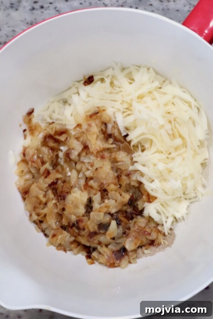 Savory French Onion Bites 4 Chopped caramelized onions and shredded cheese in a white mixing bowl on a speckled countertop, ready to be mixed into the creamy filling for crescent rolls.