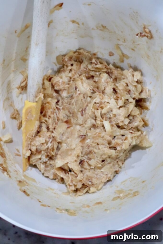 Savory French Onion Bites 5 A mixing bowl contains a creamy caramelized onion mixture with a yellow spatula in the bowl, perfectly blended and ready to spread onto crescent dough.