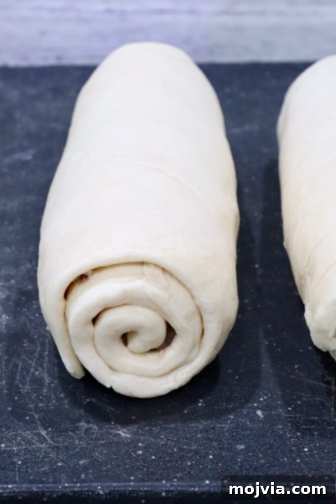 Savory French Onion Bites 7 Two neatly rolled croissant dough logs rest side by side on a dark, floured surface, filled with the savory onion and cheese mixture, ready for slicing and baking.