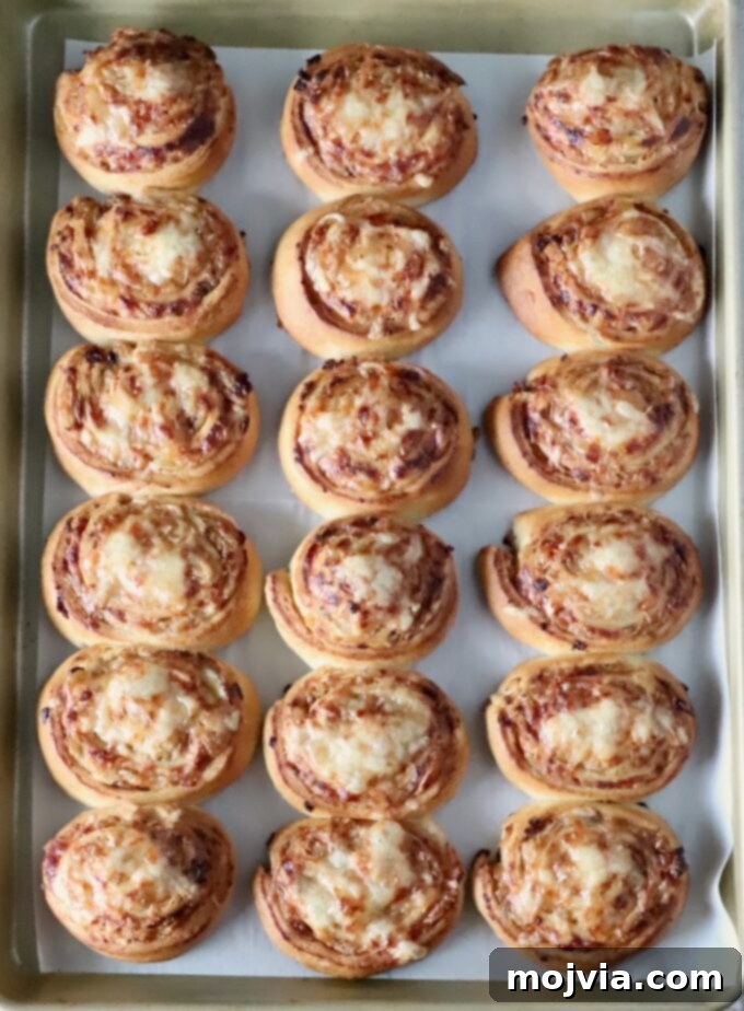 Savory French Onion Bites 9 Eighteen golden-brown cheese and caramelized onion rolls, freshly baked and perfectly arranged in three rows on a baking sheet, showcasing their crispy, flaky texture.