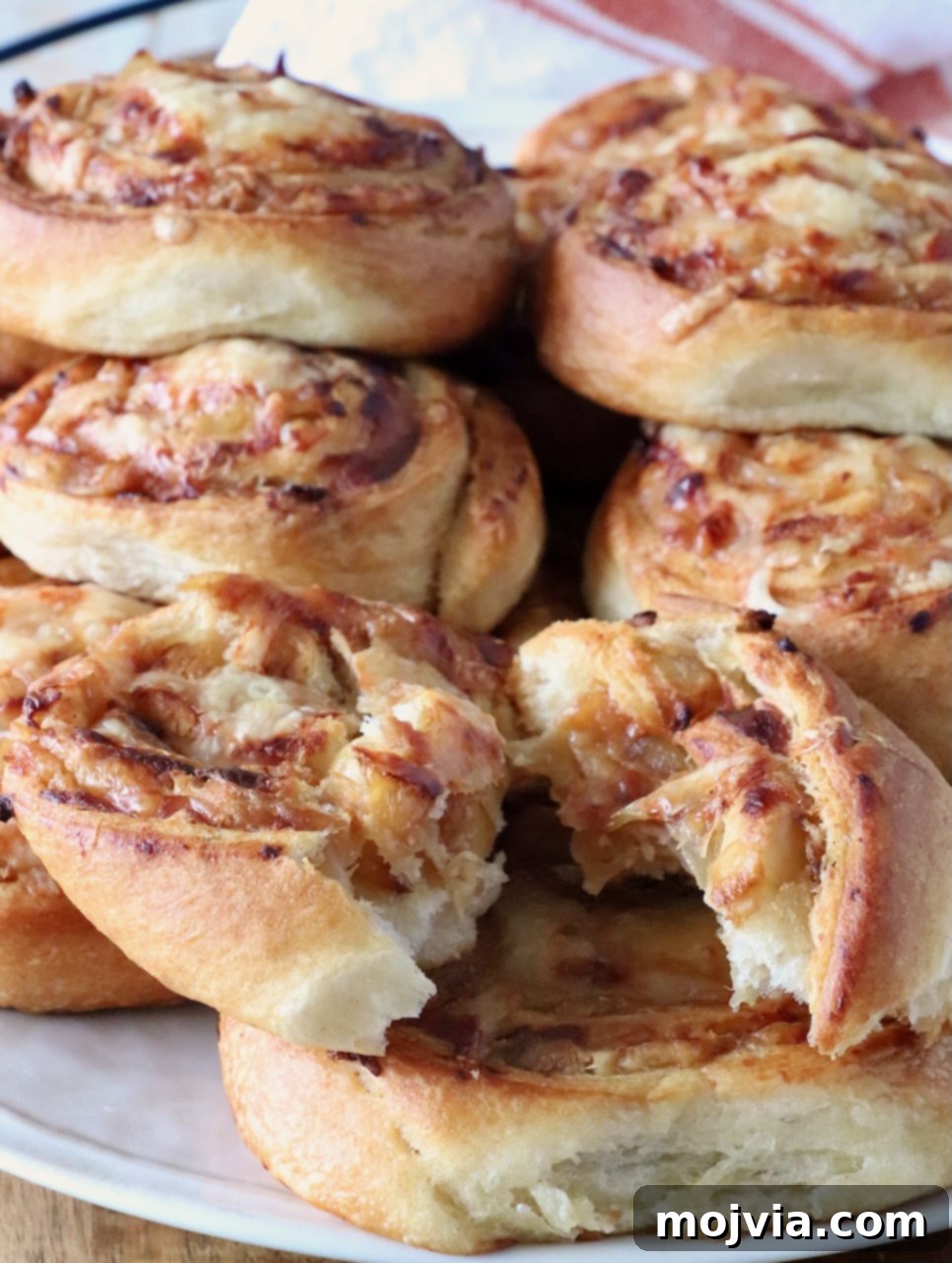 Savory French Onion Bites 10 A plate of golden-brown, onion and cheese-filled pastries stacked up on a plate. The pastries have a flaky texture, with one torn open, revealing gooey, melted cheese inside, inviting a delightful taste.