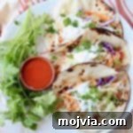 Fiery Buffalo Chicken Tacos 5 A plate of buffalo chicken tacos with a small wooden bowl of buffalo sauce on the side.