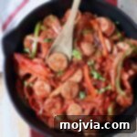 Cooked sliced bell peppers and sausage in a skillet with a wooden spoon.