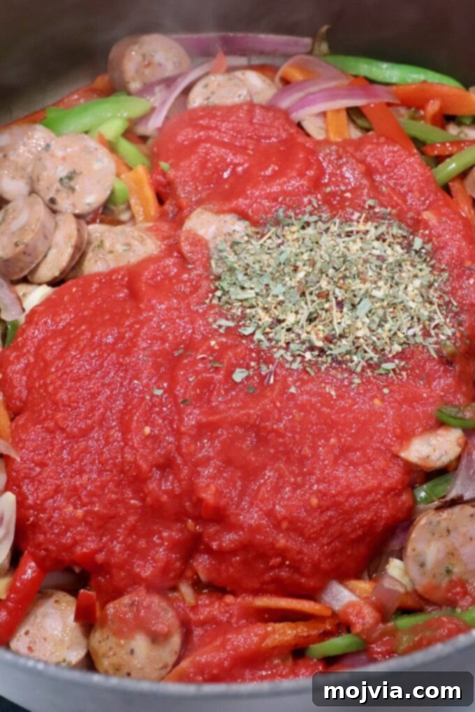 Classic Italian Sausage and Peppers 5 Crushed tomatoes and Italian seasoning added to the pan with sausage and peppers, ready to simmer.
