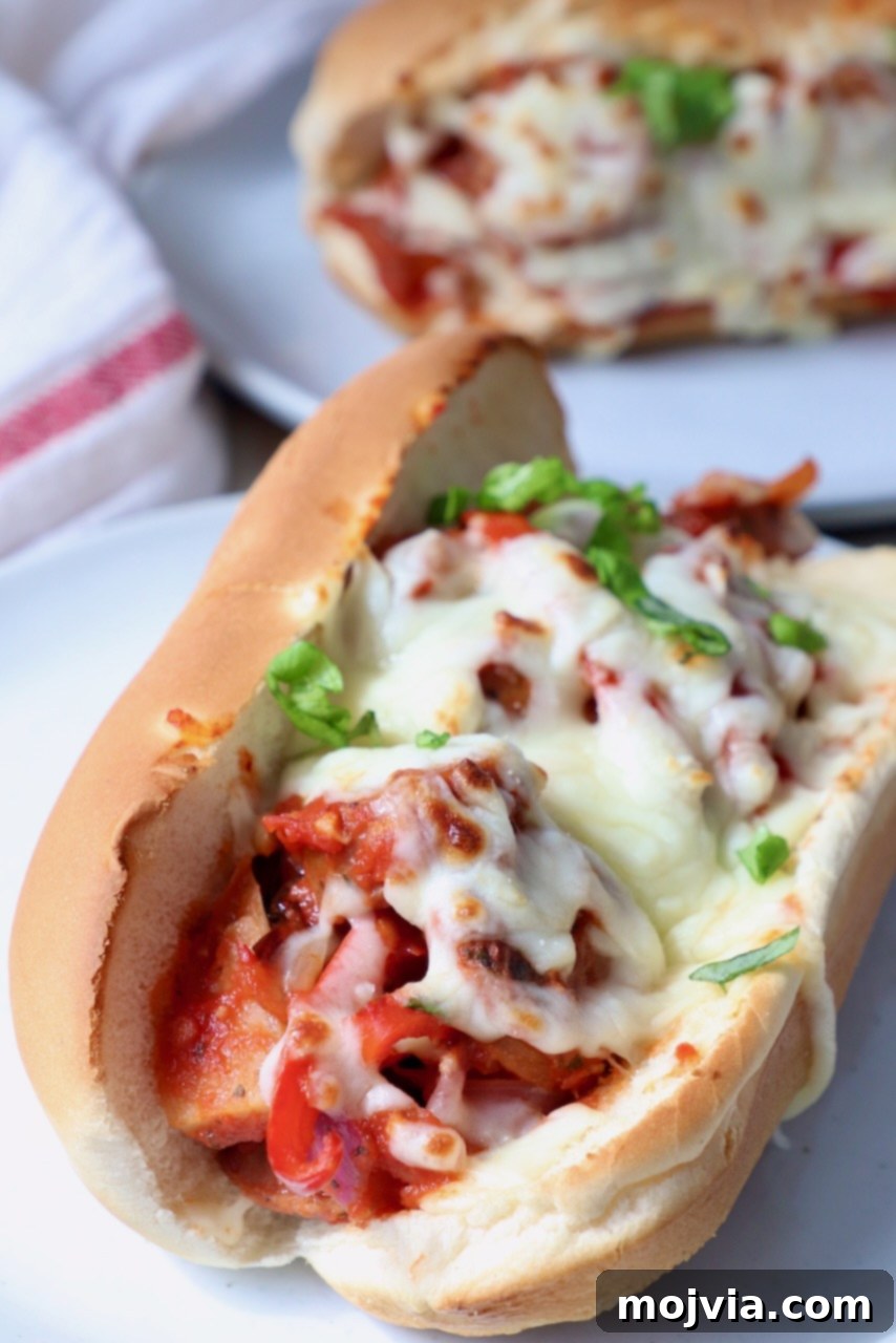 Classic Italian Sausage and Peppers 6 Sausage and peppers served in a sub sandwich, topped with melted mozzarella cheese, on a white plate.
