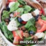 spinach salad in large bowl topped with berries, pecans and ricotta cheese