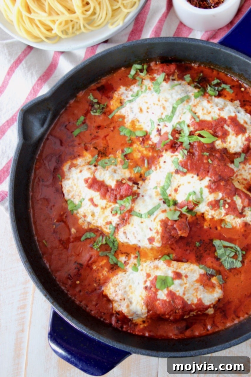 Gluten free chicken parmesan covered in marinara sauce in large cast iron skillet with a bowl of spaghetti noodles on the side, ready to serve.