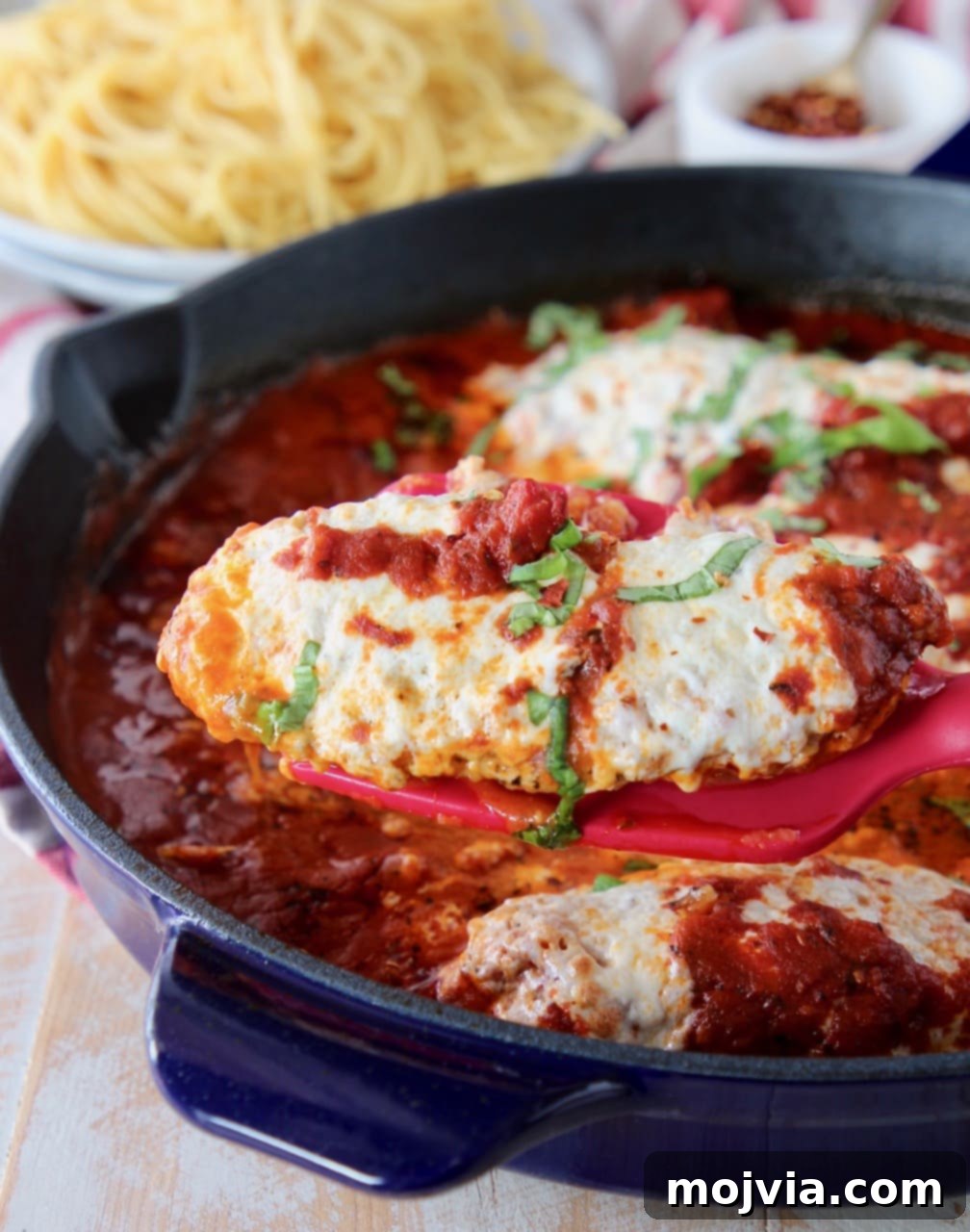Spatula holding a piece of golden-brown chicken parmesan out of a large skillet, ready to be served.