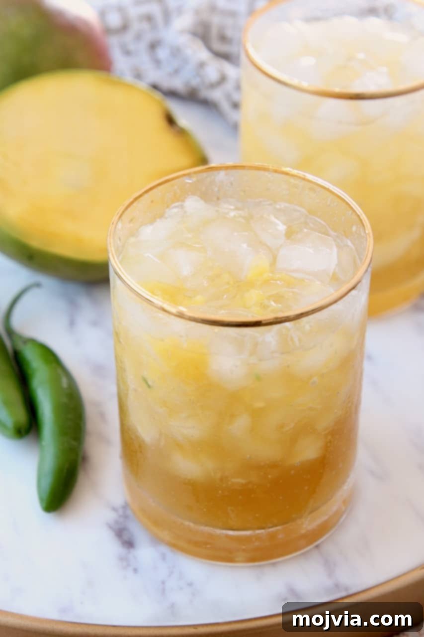 Serrano Mango Margarita Heatwave 2 Two glasses of vibrant mango margaritas garnished with lime and chili, served on a marble tray with fresh mango slices.