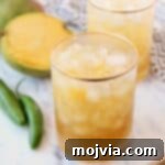 Two vibrant mango margaritas in glasses next to fresh sliced mango and a serrano chili