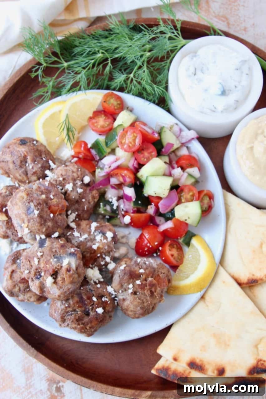Savory Greek Meatballs with Refreshing Tzatziki 2 Greek meatballs on plate with tomato cucumber salad and slices of pita bread on the side