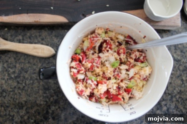 A vibrant mix of cooked couscous, flaky crab meat, diced red peppers, and chopped green onions in a mixing bowl, showcasing the colorful ingredients of the stuffing.