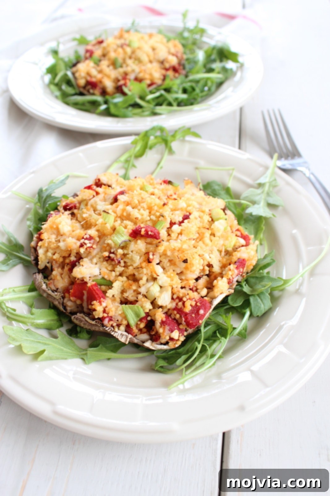 A close-up shot of a single Mediterranean Crab and Couscous Stuffed Mushroom, beautifully plated on a bed of fresh arugula, highlighting its golden-brown cap and the rich, textured filling.