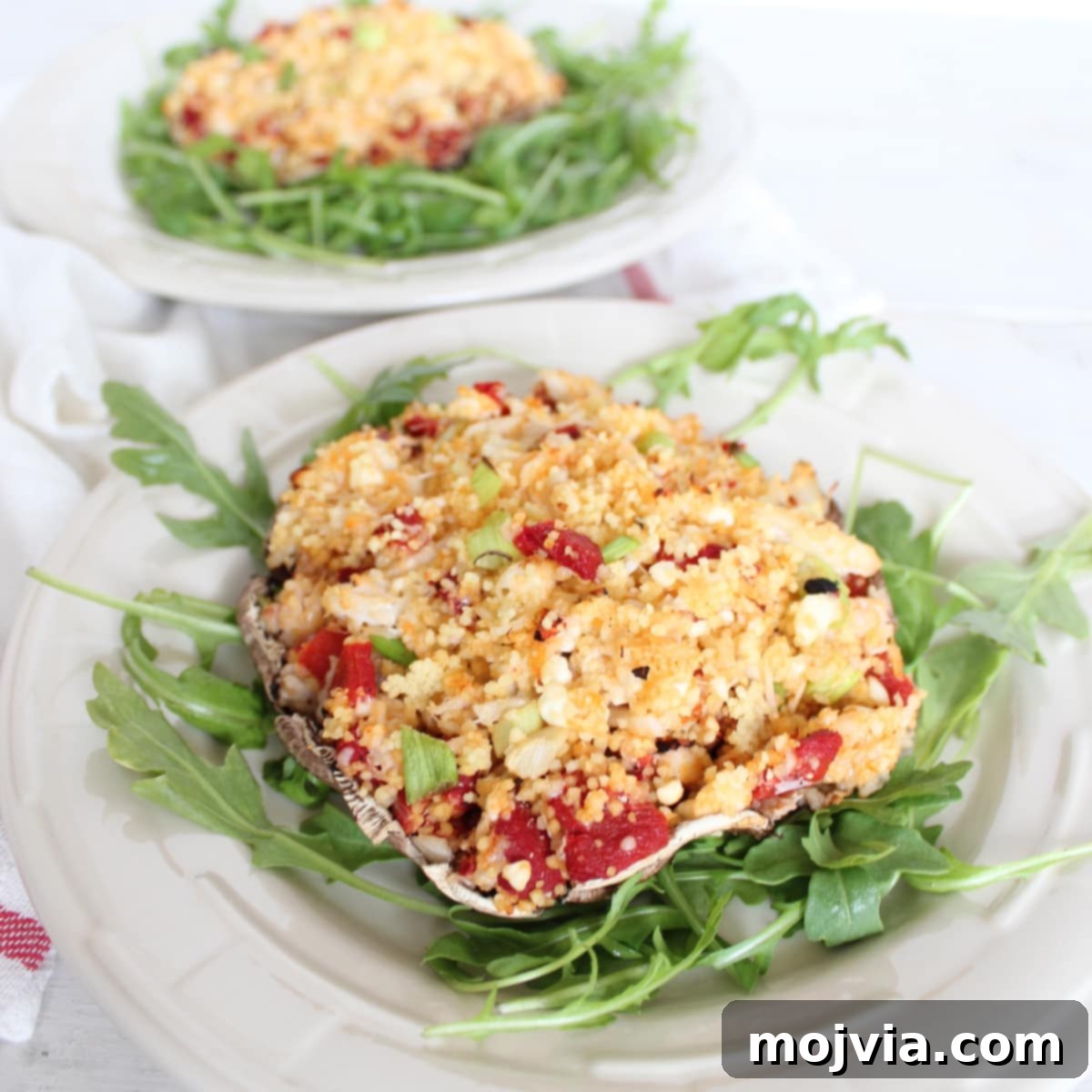 Another enticing view of a Mediterranean Crab and Couscous Stuffed Mushroom, presented on a bed of fresh arugula on a white plate, highlighting the delicious filling and perfect grilling marks.