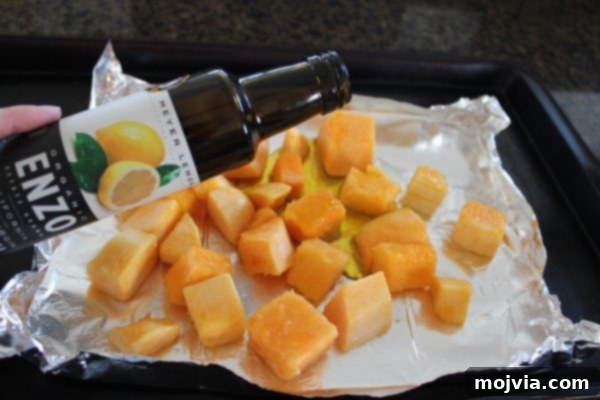 Butternut squash cubes drizzled with olive oil, ready for seasoning and roasting.