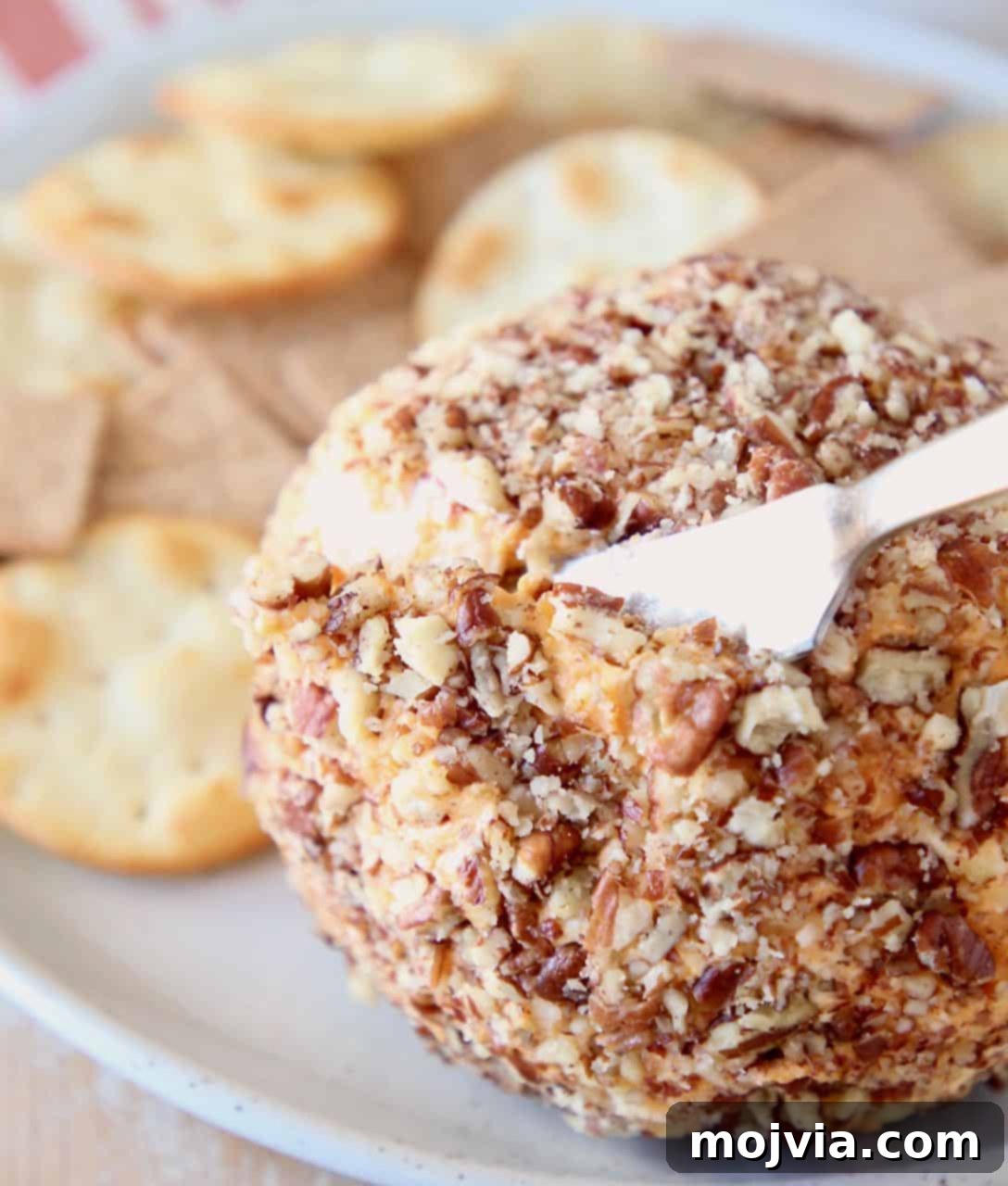 Buffalo Kicked Cheddar Cream Cheese Ball 5 A Buffalo Cheddar Cream Cheese Ball being sliced into with a cheese knife, showcasing its creamy interior.