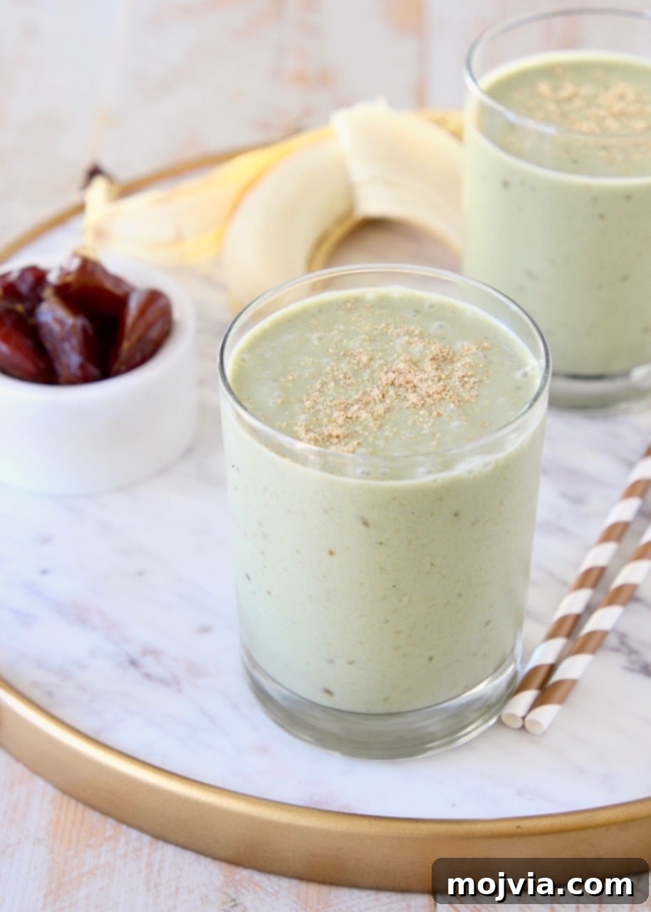 Energizing Banana Date Protein Smoothie 2 Banana protein shake in two glasses sitting on white marble tray with gold and white striped straws and peeled banana in background