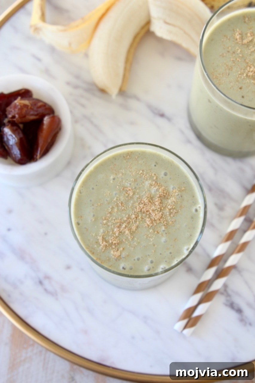 Energizing Banana Date Protein Smoothie 3 Overhead shot of two banana protein shakes topped with ground flaxseed on marble tray with gold and white striped straws and a small bowl of dates on the side