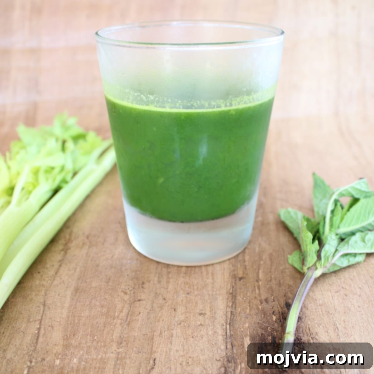 A refreshing glass of Celery Pear Healthy Green Juice garnished with a celery stalk and mint leaves.