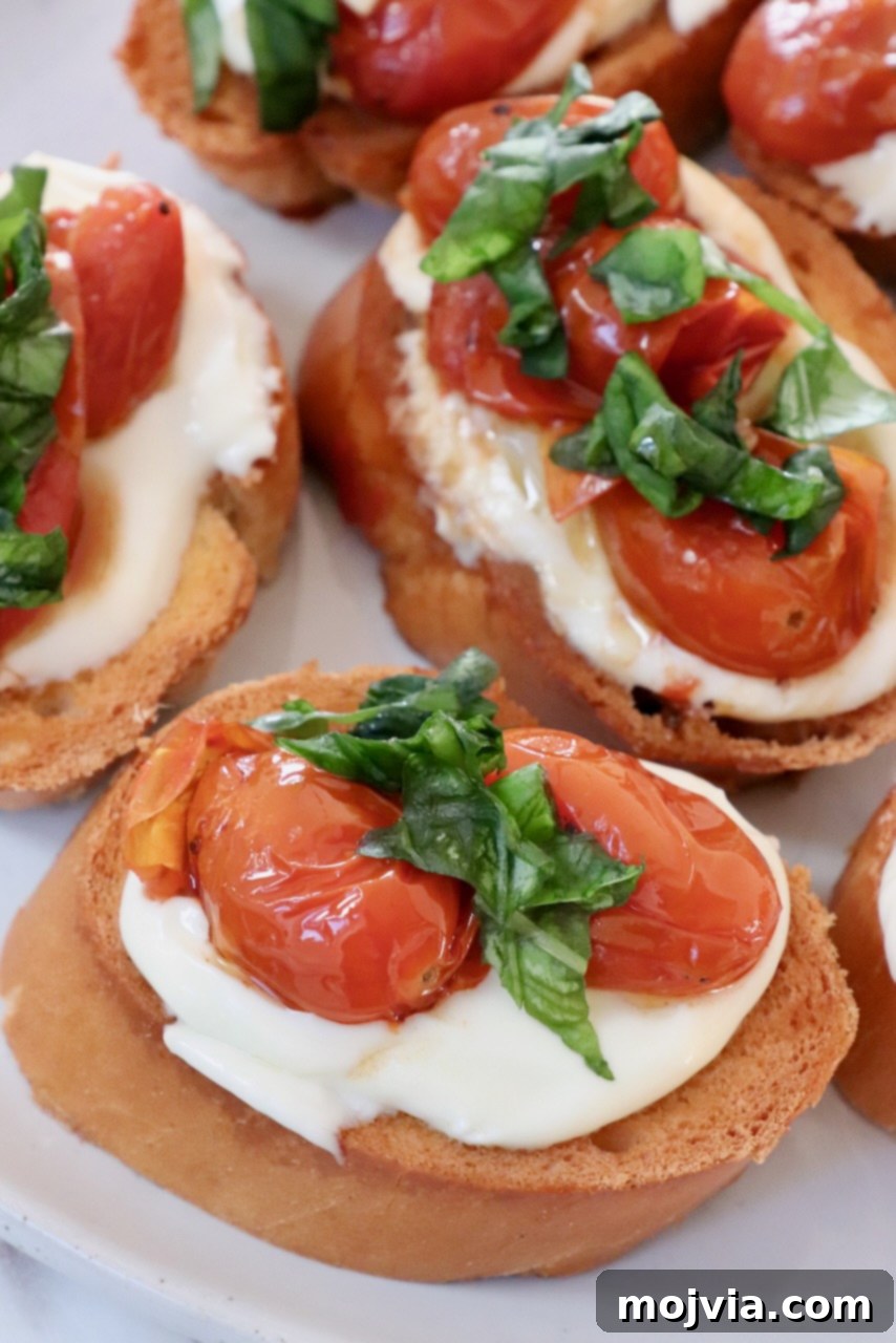 Golden Roasted Tomato Bruschetta with Whipped Ricotta 2 roasted tomatoes and whipped ricotta cheese on slices of baguette on a plate