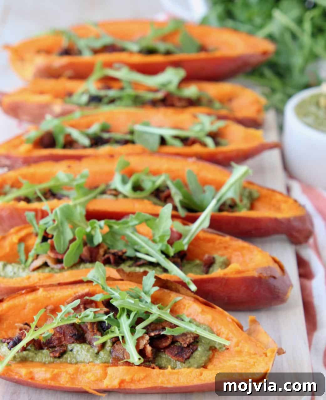 Golden Sweet Potato Skins Topped with Sage Pesto and Crispy Bacon 5 Sweet potato skins topped with arugula on wood cutting board