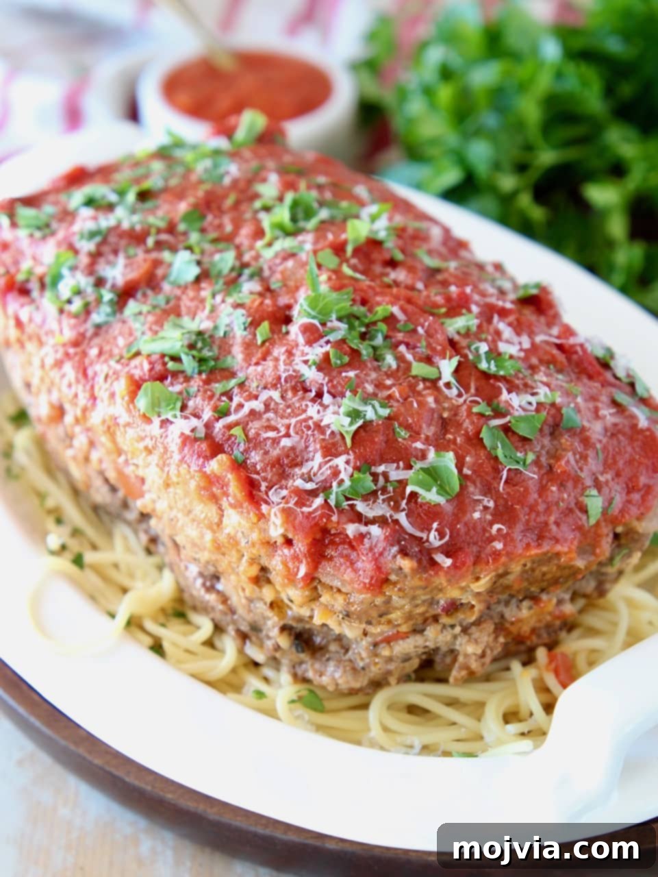 Rustic Italian Meatloaf 2 Italian meatloaf sitting on top of a bowl of spaghetti noodles, topped with fresh chopped parsley