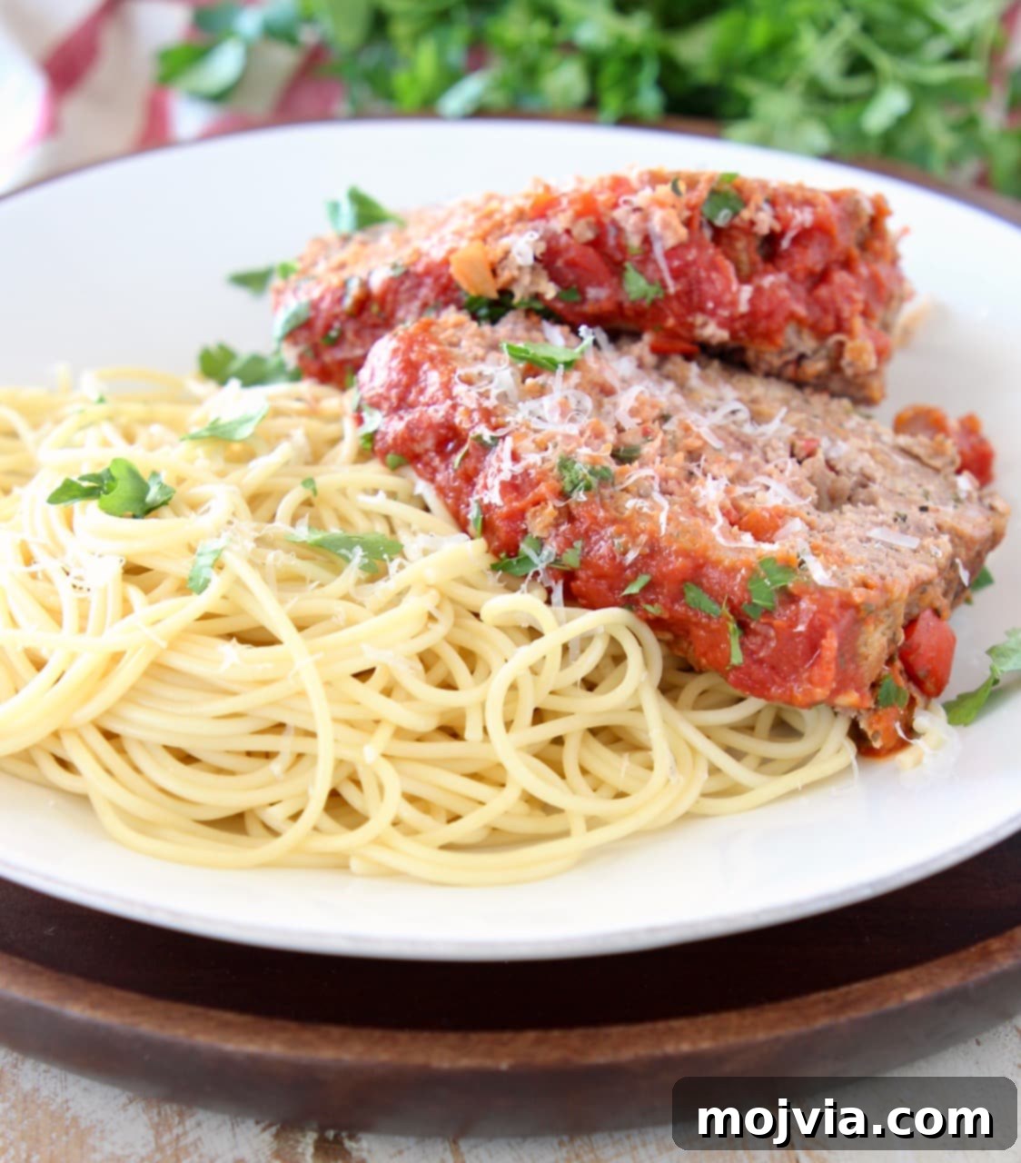 Rustic Italian Meatloaf 5 Two slices of Italian meatloaf on top of cooked spaghetti noodles on a white plate