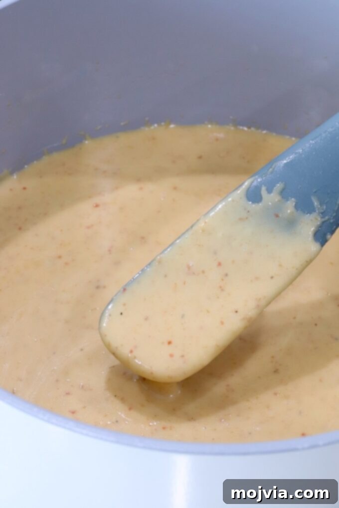 Curried Cheese Dip 7 Creamy queso in a pot with a grey spatula.