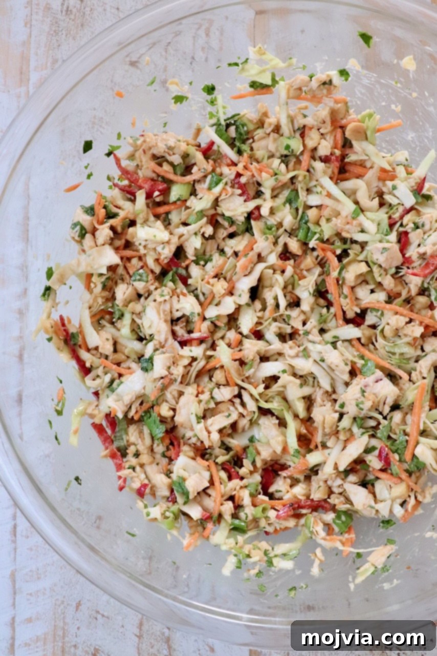 Thai-Inspired Chicken Salad Delight 4 A glass bowl filled with colorful chicken salad on a light wooden surface. The salad includes shredded cabbage, carrots, red peppers, and green herbs, giving a fresh, vibrant look.