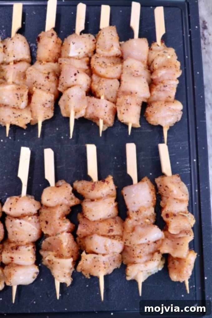 Garlic Parmesan Chicken Kebabs 4 Raw chicken skewers seasoned with spices are neatly arranged on a black cutting board. The chicken is cut into chunks.