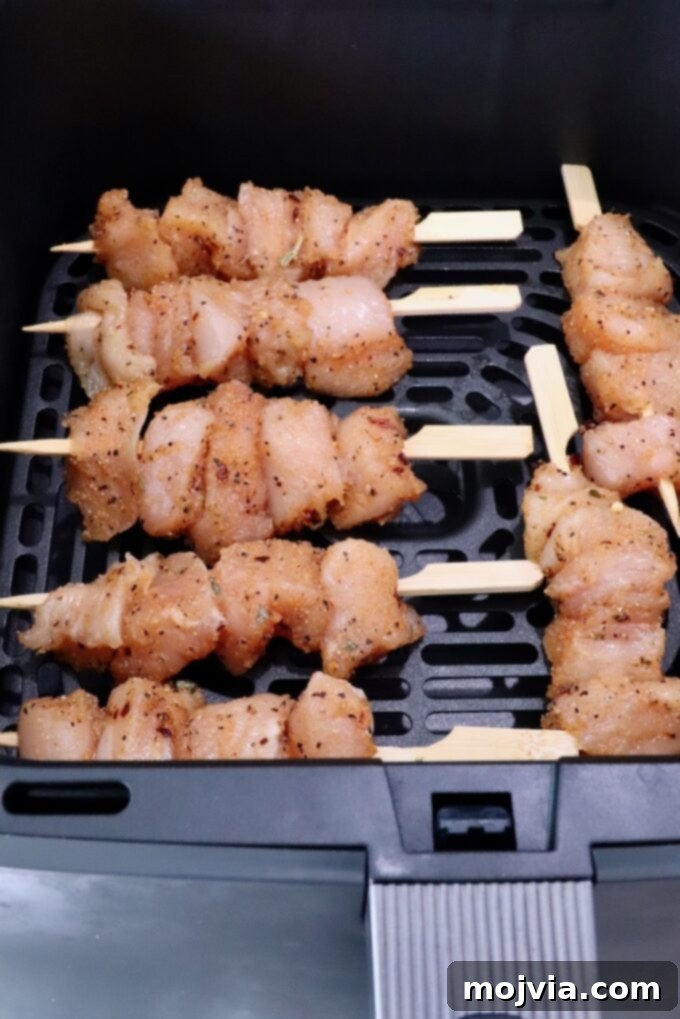 Garlic Parmesan Chicken Kebabs 5 Raw chicken skewers seasoned with spices are arranged in an air fryer basket, ready for cooking.