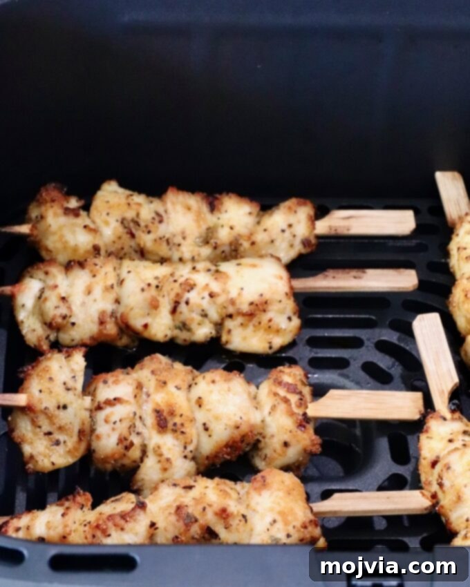 Garlic Parmesan Chicken Kebabs 6 Cooked golden brown chicken skewers seasoned with herbs placed in an air fryer basket.