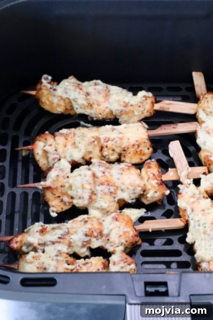 Garlic Parmesan Chicken Kebabs 7 Cooked chicken skewers topped with creamy sauce in an air fryer basket.