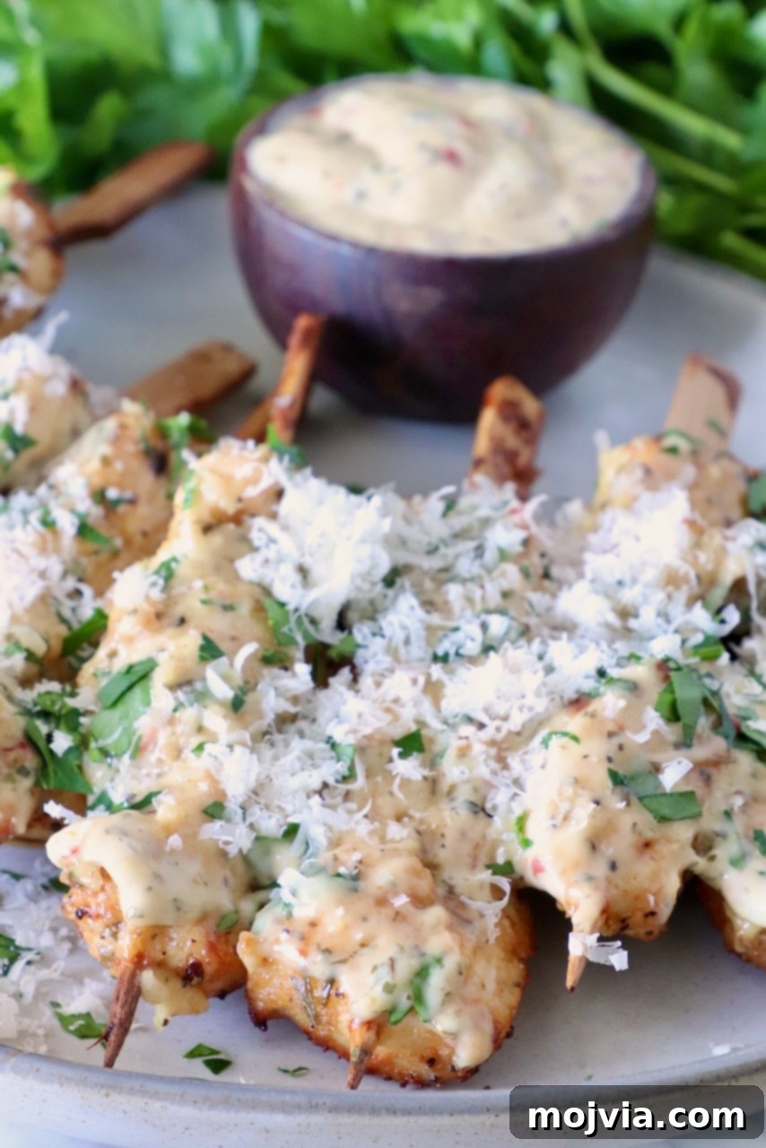 Garlic Parmesan Chicken Kebabs 8 Finished Garlic Parmesan Chicken Skewers: Air fried chicken skewers topped with creamy sauce, garnished with fresh herbs and grated cheese. A small bowl of dipping sauce is in the background.
