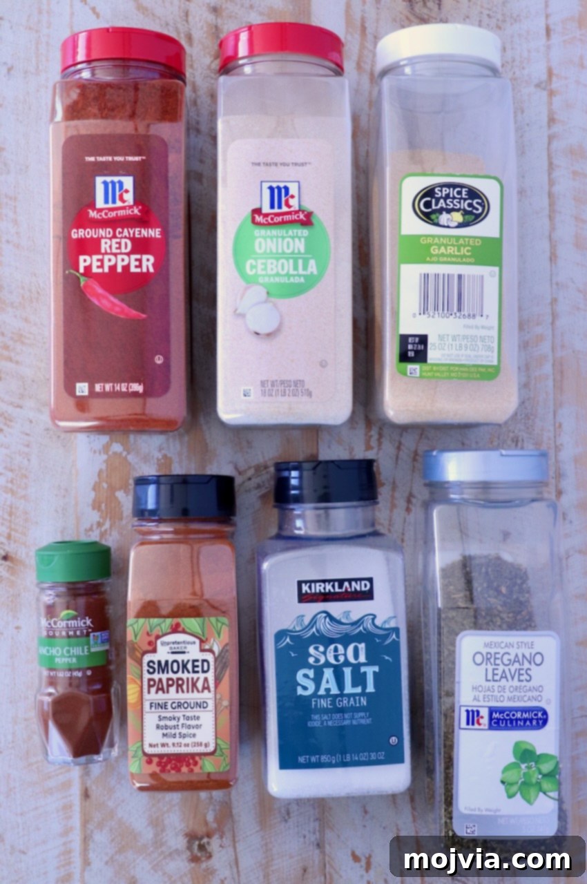 Chorizo Spice Blend 3 Assorted spice containers on a wooden surface, including red pepper, onion powder, garlic, ancho chile, paprika, sea salt, and oregano.