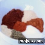 Chorizo Spice Blend 6 A white bowl containing vibrant heaps of spices, including red chili powder, paprika, oregano, and garlic powder, arranged in a colorful circle.