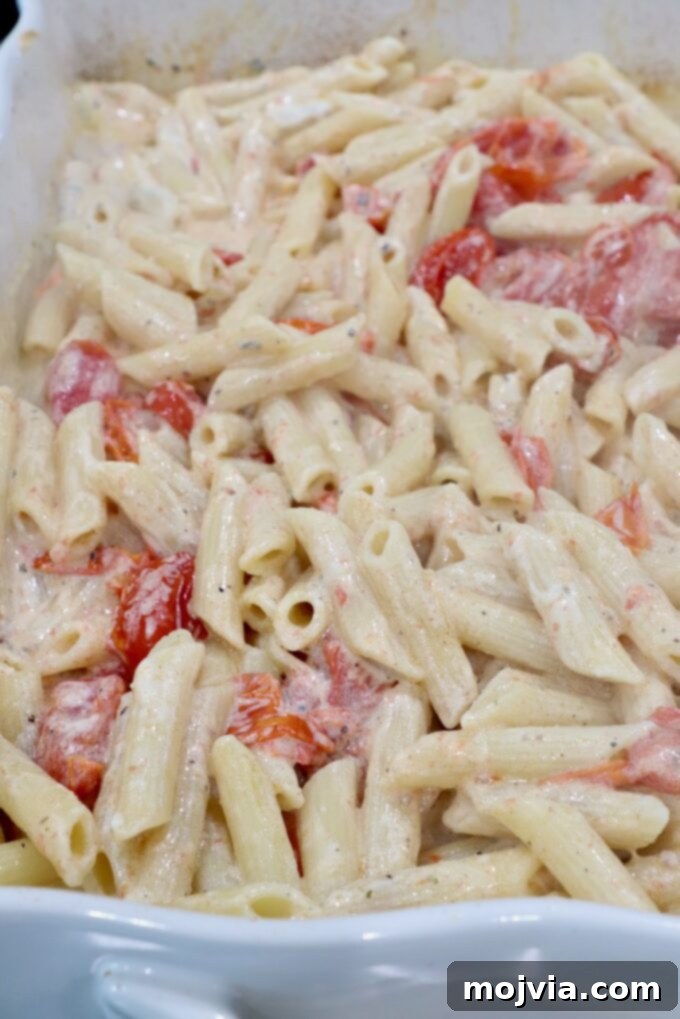 Penne pasta in a creamy sauce with cherry tomatoes in a baking dish.