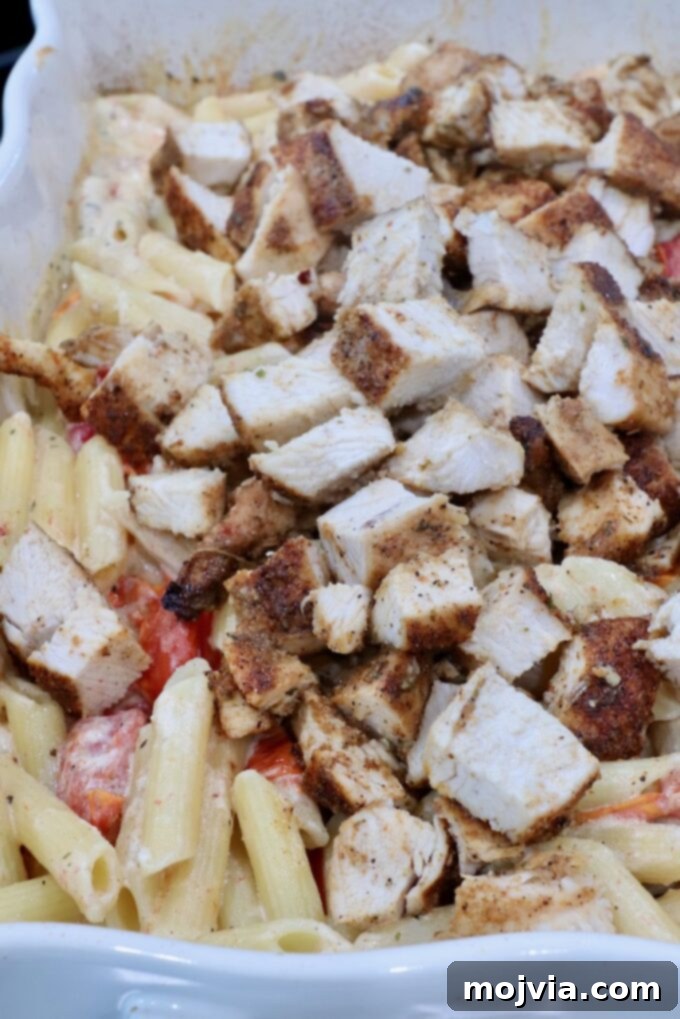Diced cooked chicken on top of pasta in a baking dish.