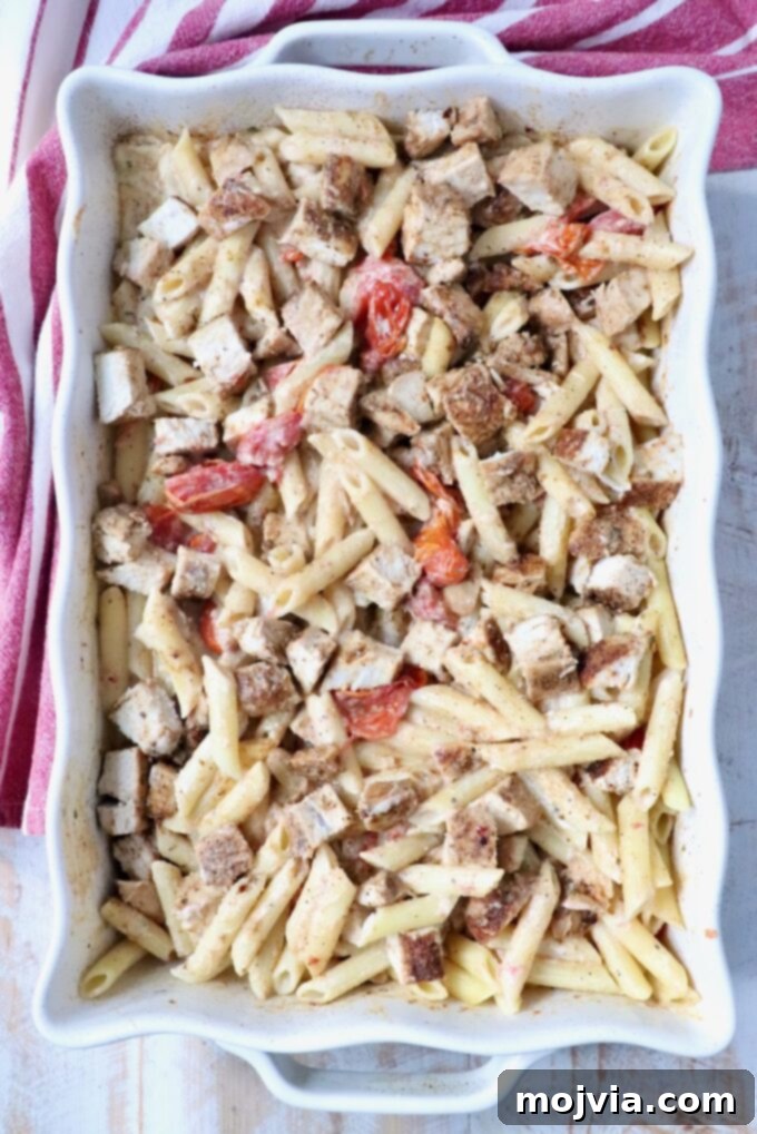 Penne pasta in a creamy sauce with roasted tomatoes and diced chicken in a baking dish.