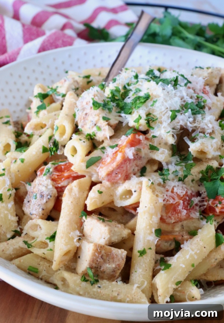 A creamy pasta dish with penne, diced chicken, cherry tomatoes, and parsley, topped with grated cheese.