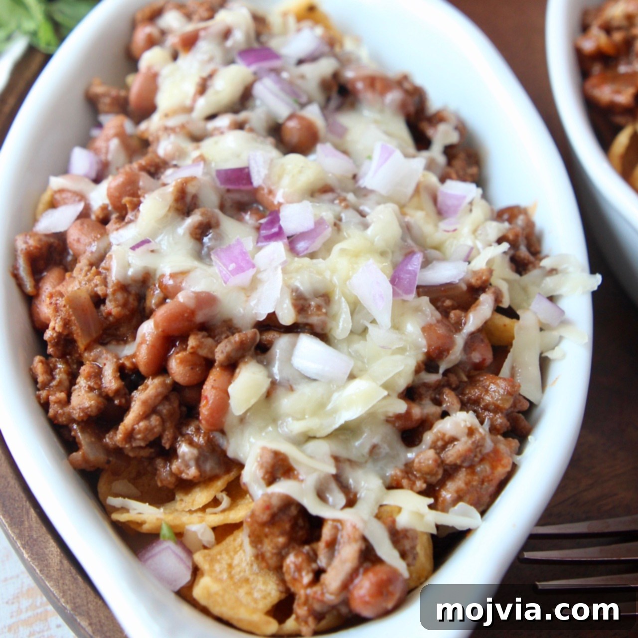 frito chili pie topped with cheese and diced red onion