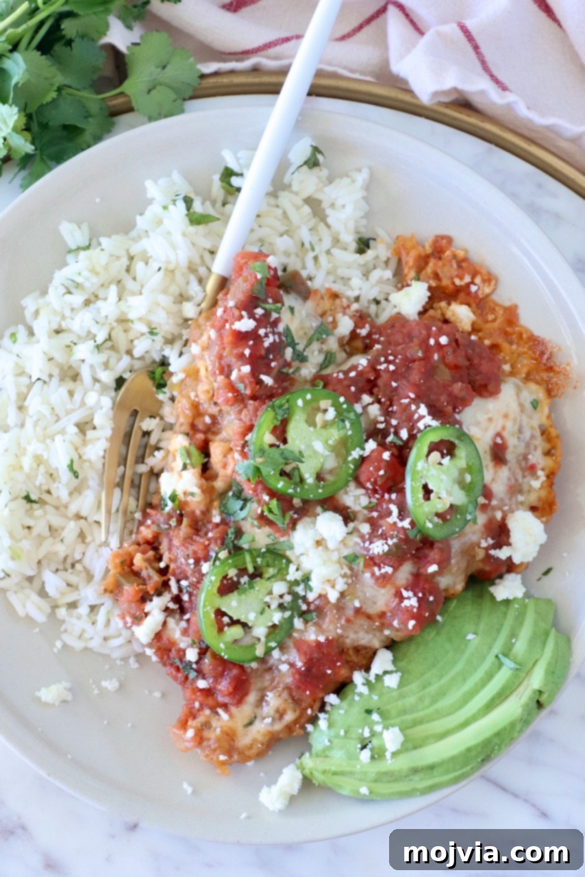 Fiesta Chicken Parmesan 2 A plate of Mexican chicken parmesan topped with salsa, jalapeño slices, and cheese, served with cilantro rice and avocado slices on the side.