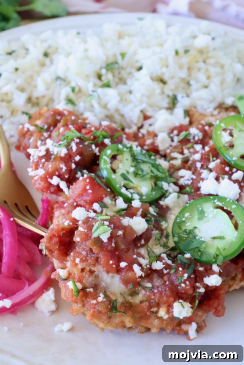 Fiesta Chicken Parmesan 10 A plate with rice and Mexican chicken parmesan, topped with sliced jalapeños and crumbled cheese, garnished with cilantro and a side of pickled onions