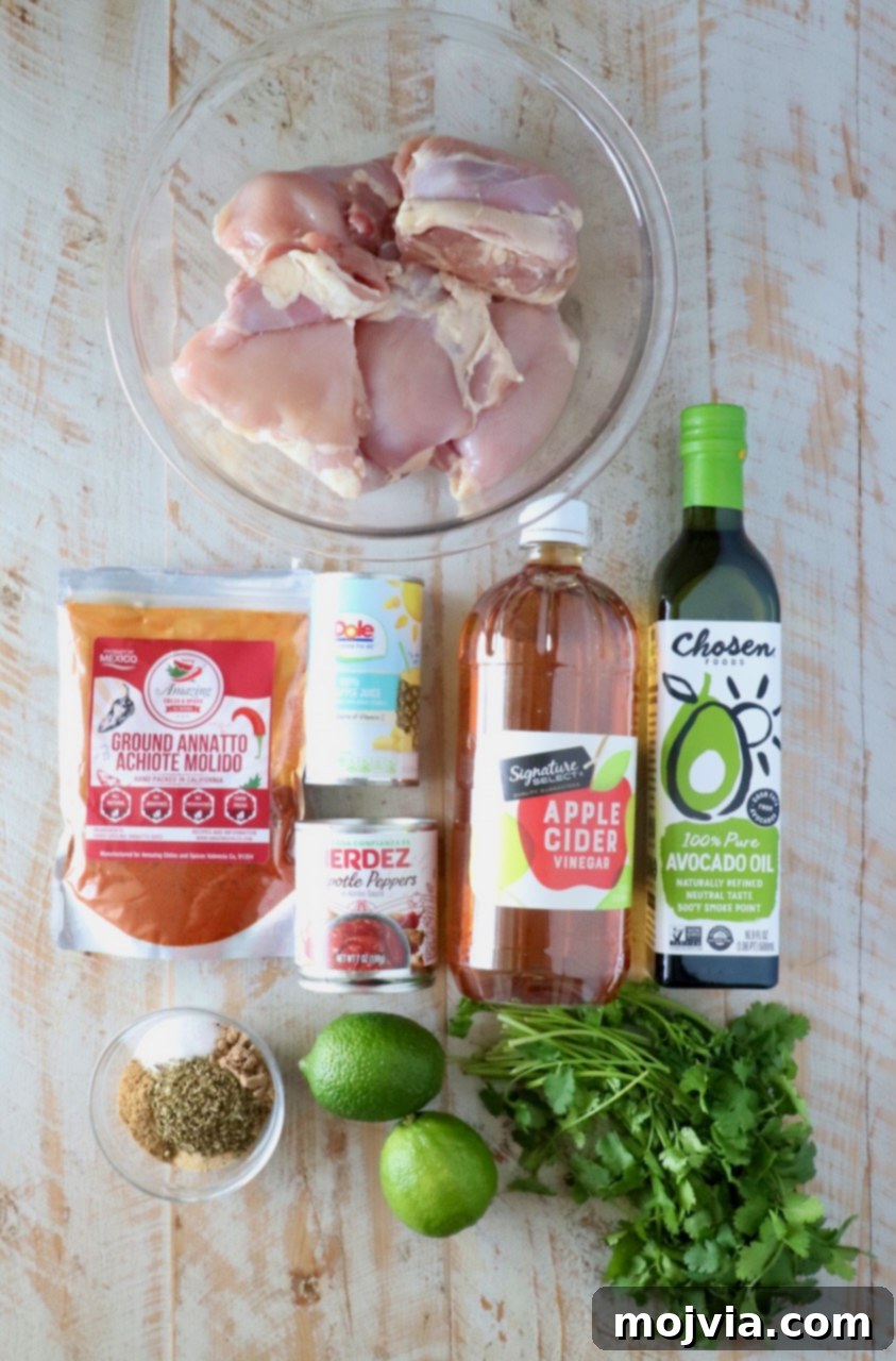 Vibrant Al Pastor Chicken 3 Raw chicken thighs in a bowl surrounded by ground annatto, pineapple juice, chipotle peppers, apple cider vinegar, avocado oil, lime, cilantro, and various spices, all prepped for the marinade.