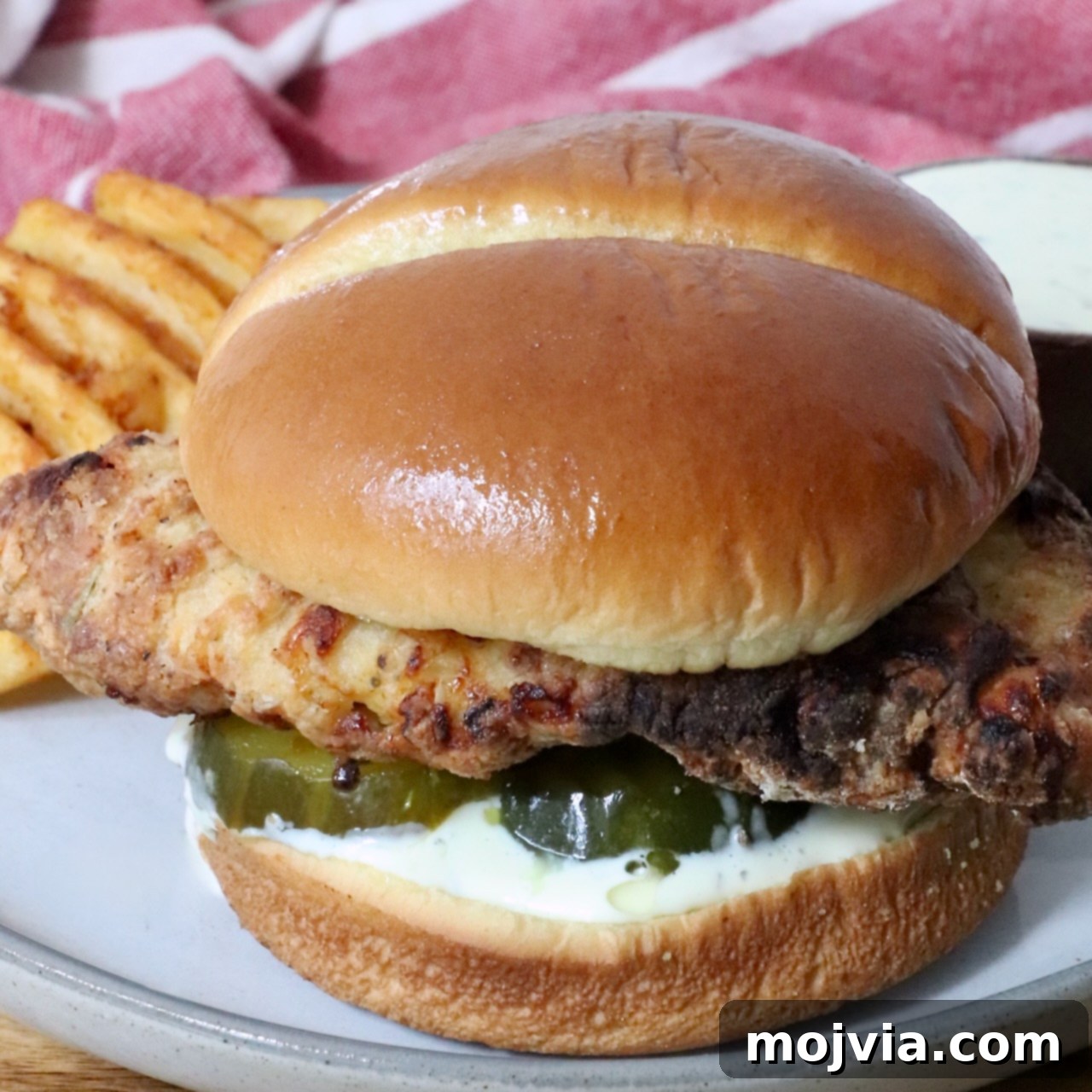 Crispy Air-Fried Chicken Sandwich 2 A crispy air fried chicken sandwich on a soft bun with pickles and creamy sauce, served with waffle fries on a plate.