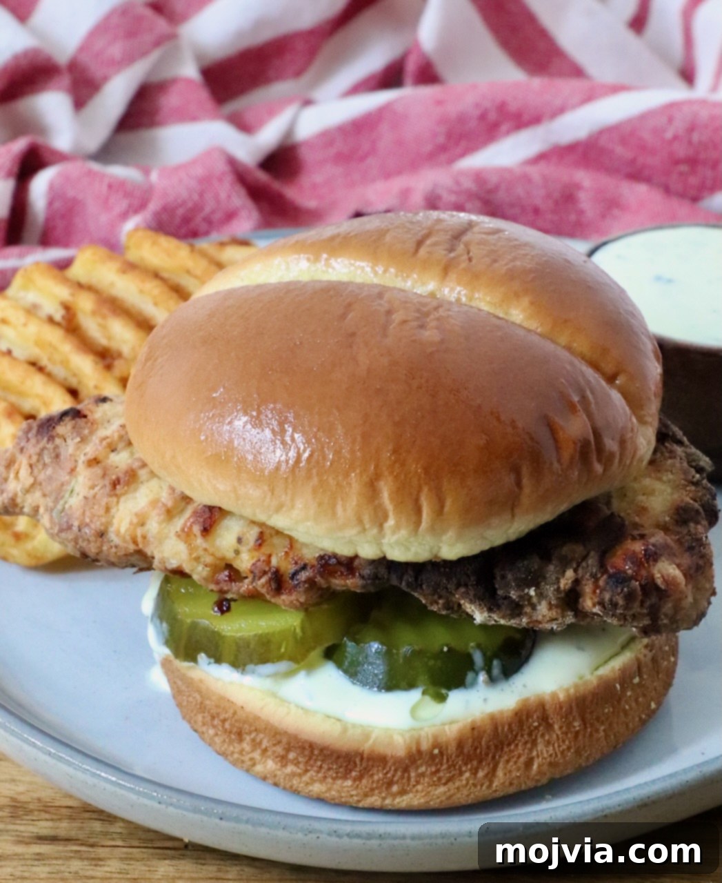 Crispy Air-Fried Chicken Sandwich 13 A crispy air fried chicken sandwich on a soft bun with pickles and creamy sauce, served with waffle fries on a plate.