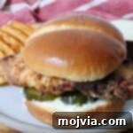 Crispy Air-Fried Chicken Sandwich 14 A crispy air fried chicken sandwich on a soft bun with pickles and creamy sauce, served with waffle fries on a plate.