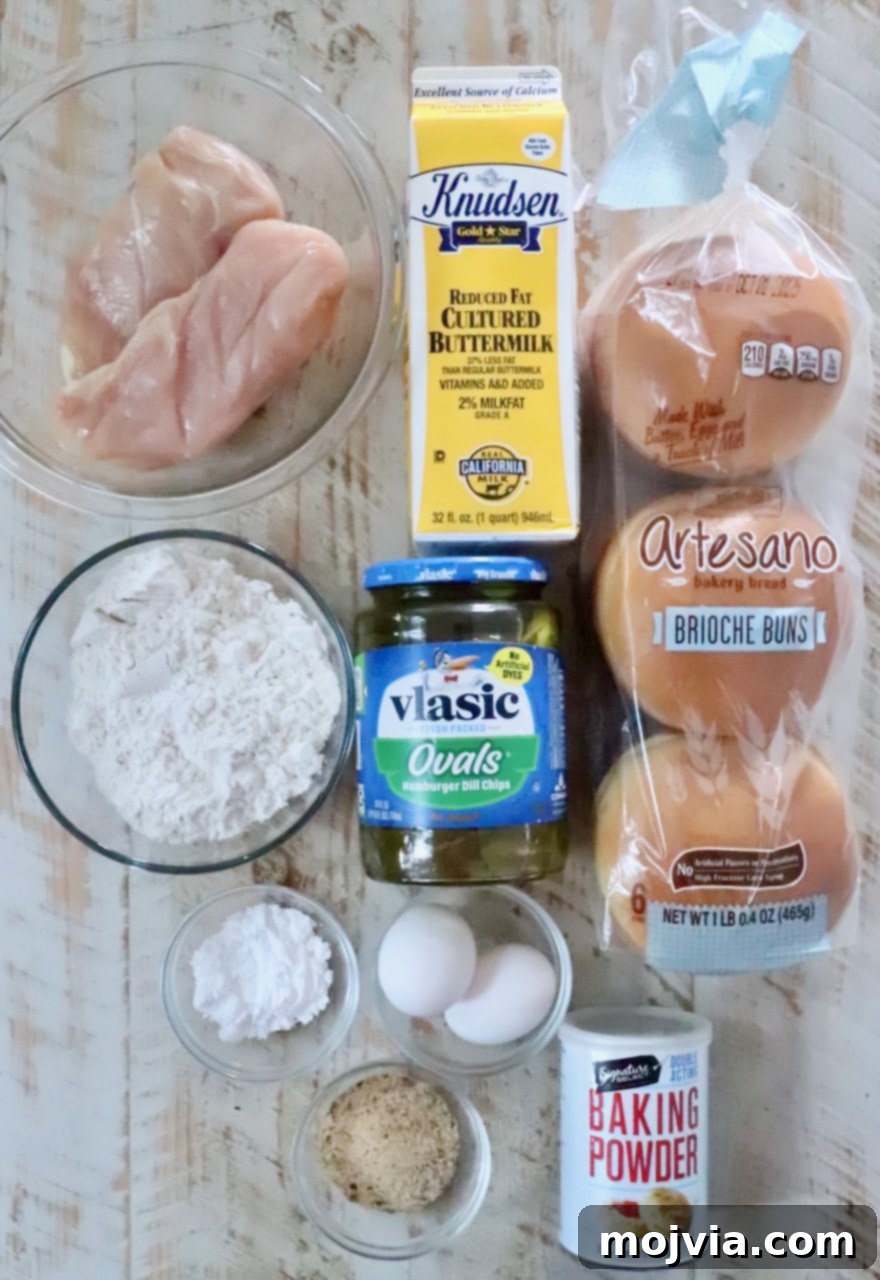 Crispy Air-Fried Chicken Sandwich 3 Ingredients for a chicken sandwich are neatly arranged: raw chicken, buttermilk, brioche buns, flour, pickles, eggs, baking powder, and chicken seasoning.