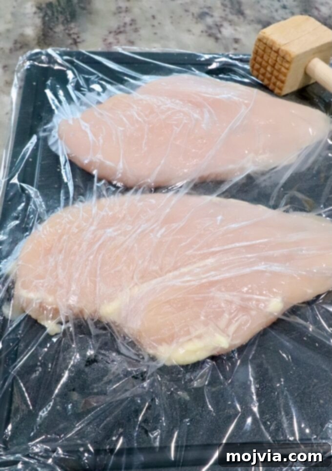 Crispy Air-Fried Chicken Sandwich 4 chicken breasts on a cutting board under a piece of plastic wrap