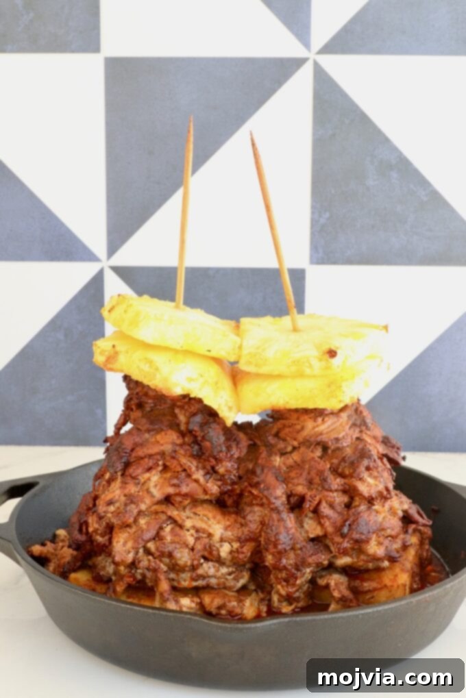 Sweet & Spicy Al Pastor Pork 6 A stack of marinated, cooked pork layered on skewers, topped with pineapple slices, in a cast iron skillet.